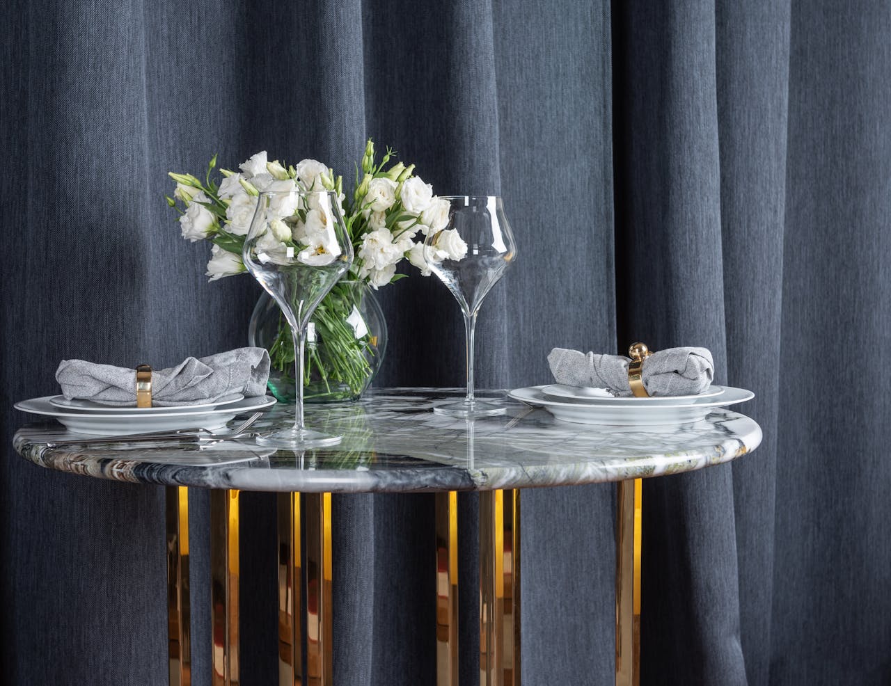 Glasses and plates arranged with bunch of flowers in vase on marble table